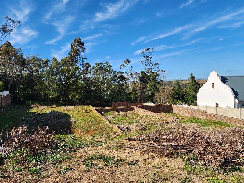 A vacant residential plot featuring existing brick foundation walls, surrounded by established trees and neighboring property boundaries.
