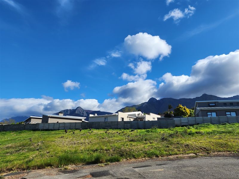 A view of a vacant residential plot featuring a precast concrete boundary wall with mountain views in the background.