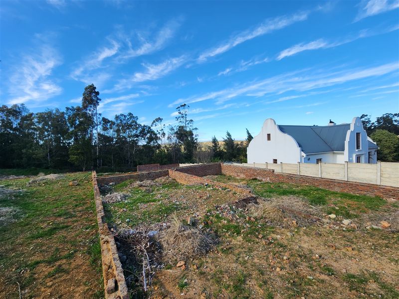 A vacant residential plot featuring existing brick foundation walls and a precast concrete boundary wall, set in a quiet neighborhood.