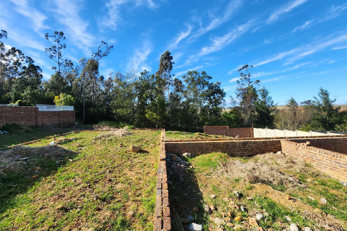 A vacant residential plot featuring partial brick foundation walls and perimeter boundary fencing, set against a backdrop of mature trees.