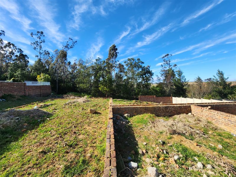 A vacant residential plot featuring partial brick foundation walls and perimeter boundary fencing, set against a backdrop of mature trees.