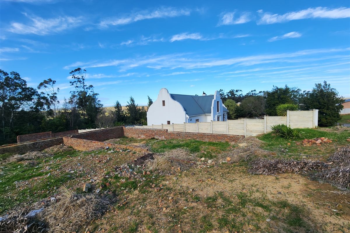 A view of a vacant residential plot featuring partial brick wall foundations and boundary fencing, with an adjacent house visible in the background.