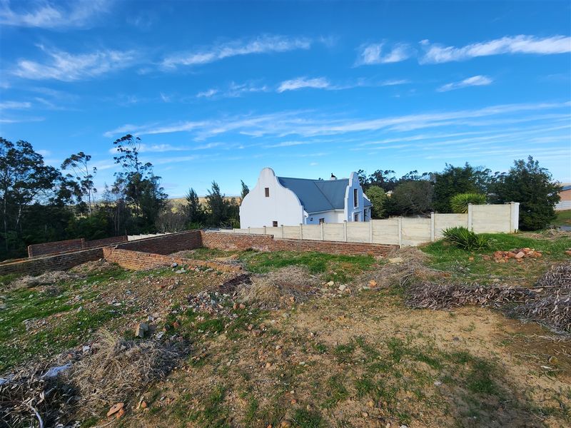 A view of a vacant residential plot featuring partial brick wall foundations and boundary fencing, with an adjacent house visible in the background.