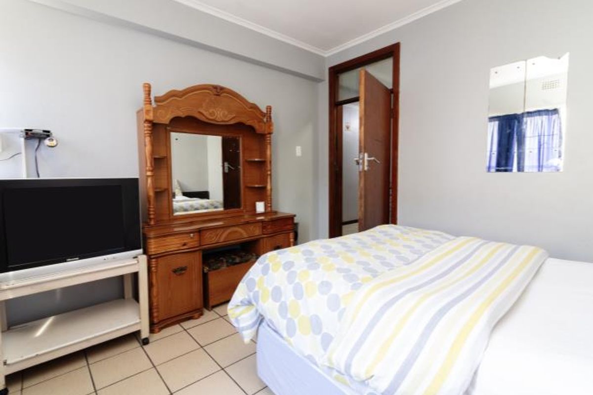 A bedroom featuring tiled flooring and neutral wall finishes, providing a functional space with direct access to the hallway.