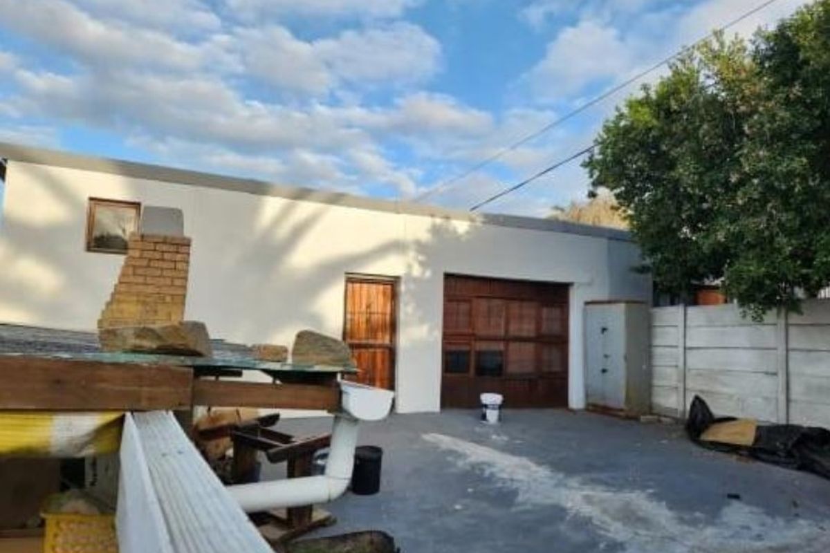 Rear exterior view showing a garage, brick chimney, and concrete paved area with boundary walling.