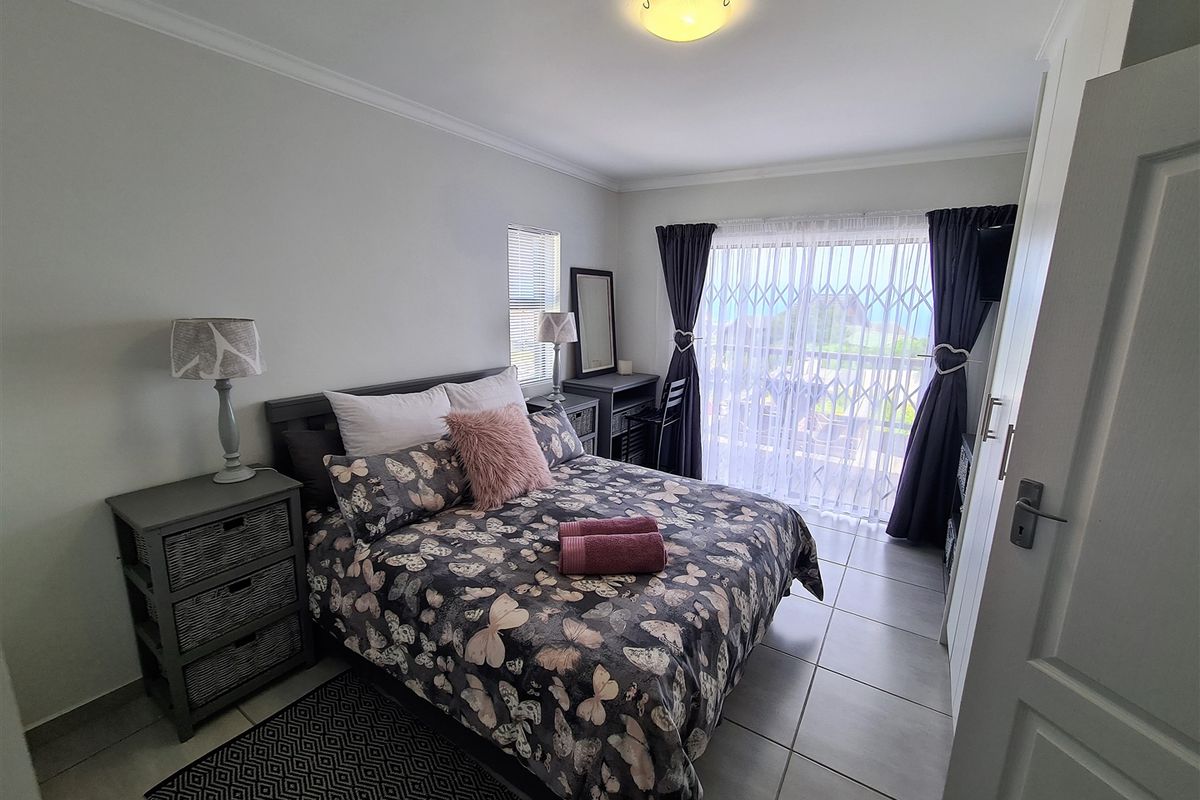 A well-maintained bedroom featuring tiled flooring, a built-in cupboard, and a sliding glass door with a security gate leading to an outdoor area.