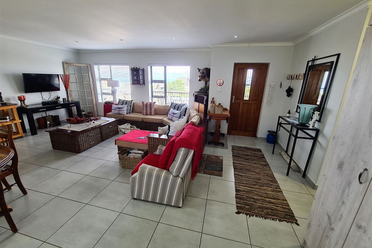 Spacious open-plan living area featuring neutral tiled flooring, recessed lighting, and large windows providing natural light and access to the entrance.