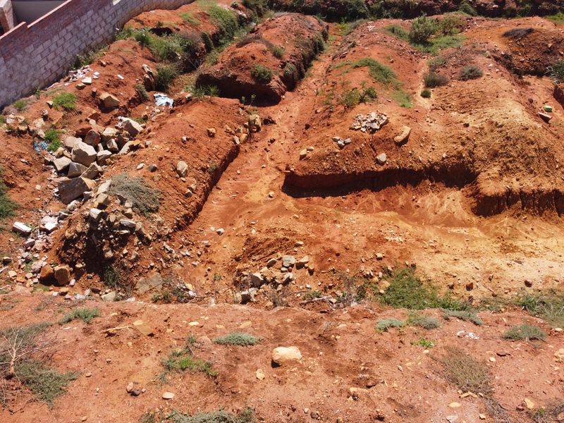 Aerial view of a vacant residential plot featuring excavated earth and a partial boundary wall, ready for development.
