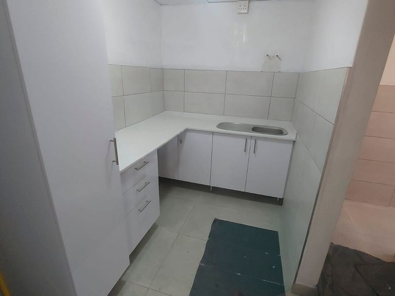 A compact, empty kitchen area featuring white built-in cabinetry, a stainless steel sink, and neutral tiled finishes, ready for customization.
