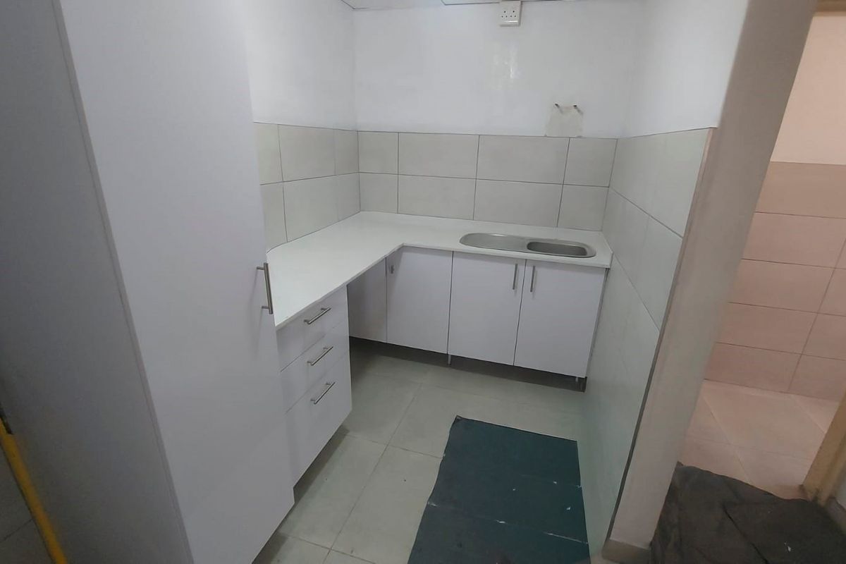 A compact, empty kitchen area featuring white built-in cabinetry, a stainless steel sink, and neutral tiled finishes, ready for customization.