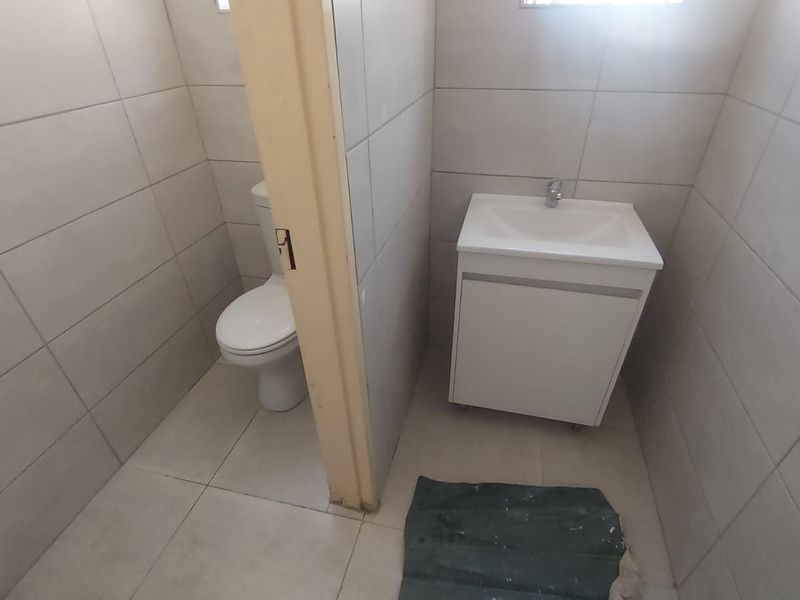A functional bathroom featuring a toilet, a modern vanity cabinet with a washbasin, and neutral floor-to-ceiling wall tiling.