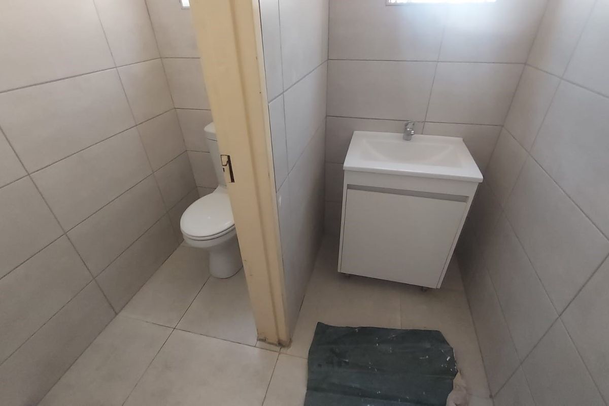 A functional bathroom featuring a toilet, a modern vanity cabinet with a washbasin, and neutral floor-to-ceiling wall tiling.