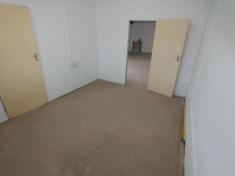 An empty, utilitarian room featuring plain white walls, internal doors, and unfinished flooring, suitable for storage or office use.