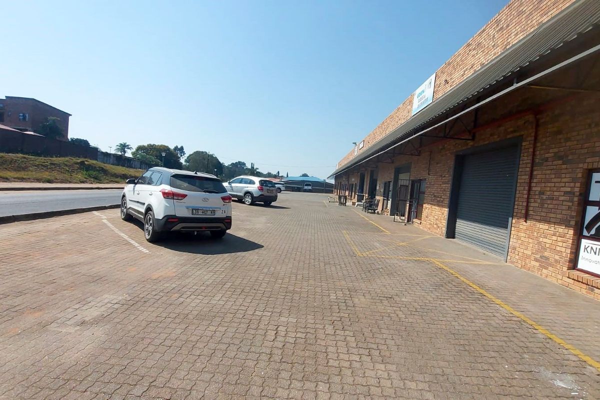 Exterior view of a retail property featuring a brick facade, roller shutter doors, and a paved parking area.
