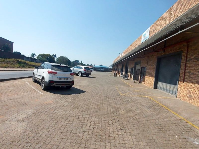 Exterior view of a retail property featuring a brick facade, roller shutter doors, and a paved parking area.