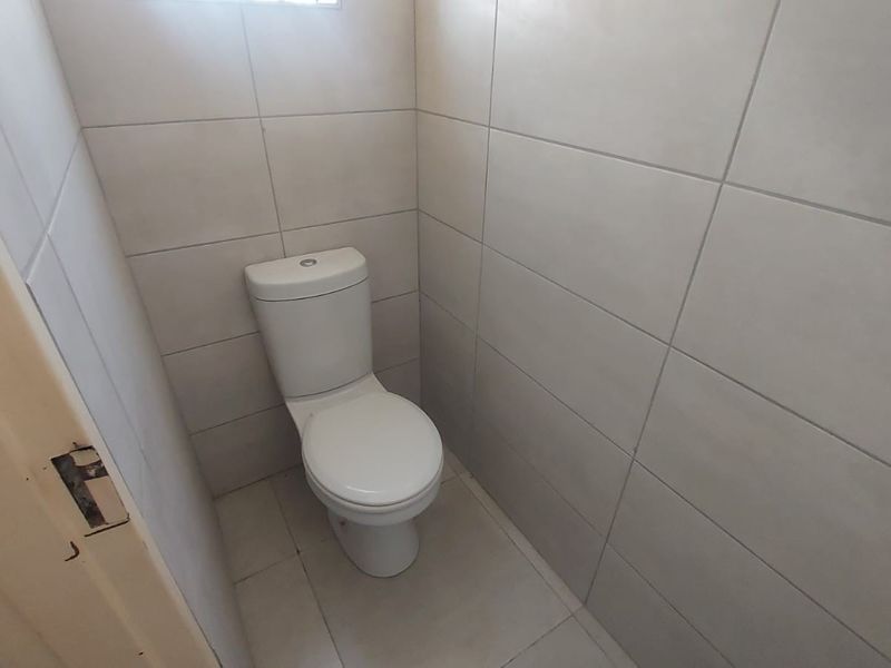 A compact bathroom featuring a white toilet and neutral ceramic wall and floor tiling.