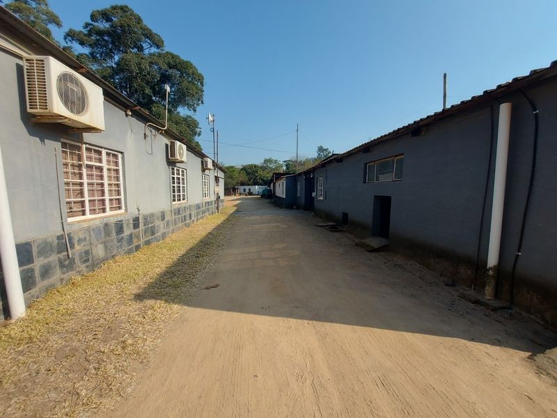 Exterior view of a commercial property featuring a dirt driveway between two single-story buildings with mounted air conditioning units and tiled facade bases.