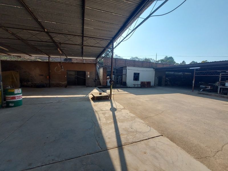 Spacious industrial yard featuring a large covered area with corrugated metal roofing, concrete flooring, and secure brick boundary walls.