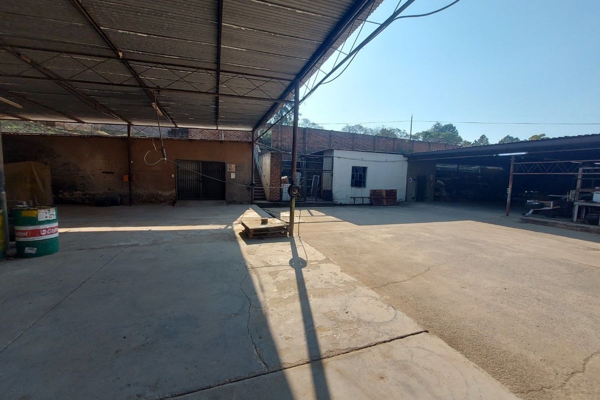 Spacious industrial yard featuring a large covered area with corrugated metal roofing, concrete flooring, and secure brick boundary walls.