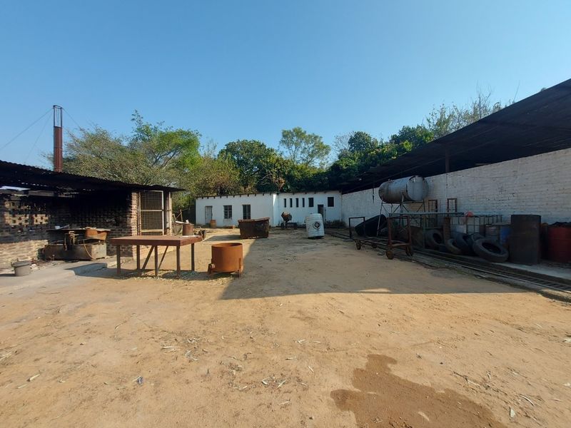 Rear yard area of a business property featuring open-air workspace, covered storage structures, and basic brick and metal construction.