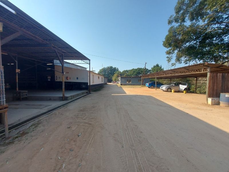Exterior view of a commercial property featuring a large covered loading area, open dirt yard, and a separate covered parking structure.