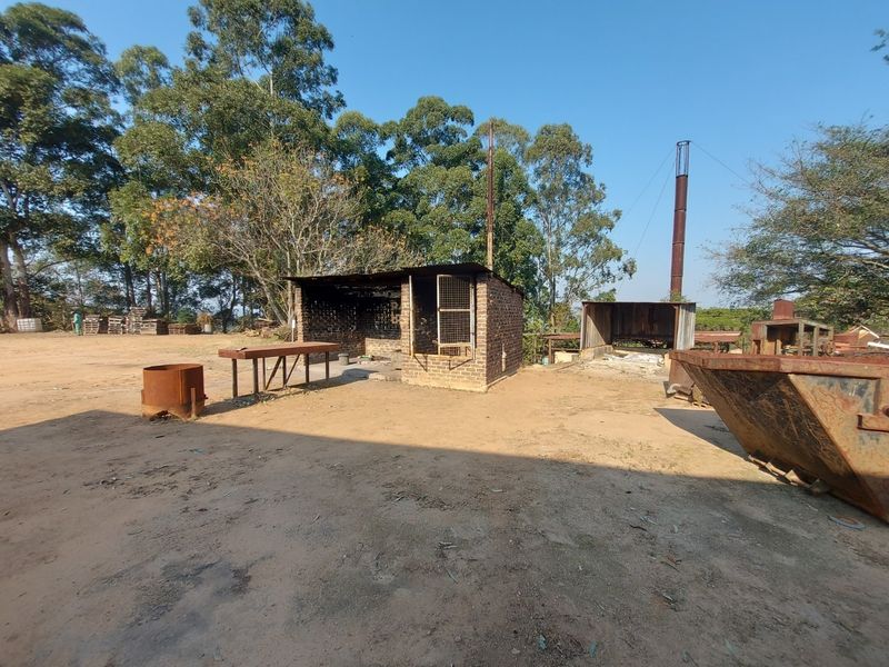 Outdoor utility area featuring a brick structure, metal chimney stack, and open workspace on a dirt lot, suitable for industrial or storage purposes.