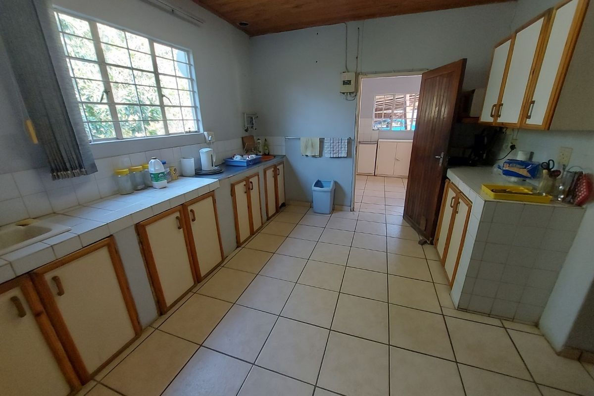 A functional kitchen featuring tiled countertops, built-in wooden cabinetry, and ceramic floor tiles, with a timber ceiling and direct access to an adjacent utility area.