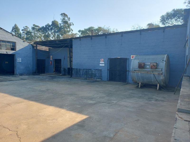 Industrial rear yard area featuring a concrete surface, blue painted masonry walls, and a large metal storage tank.