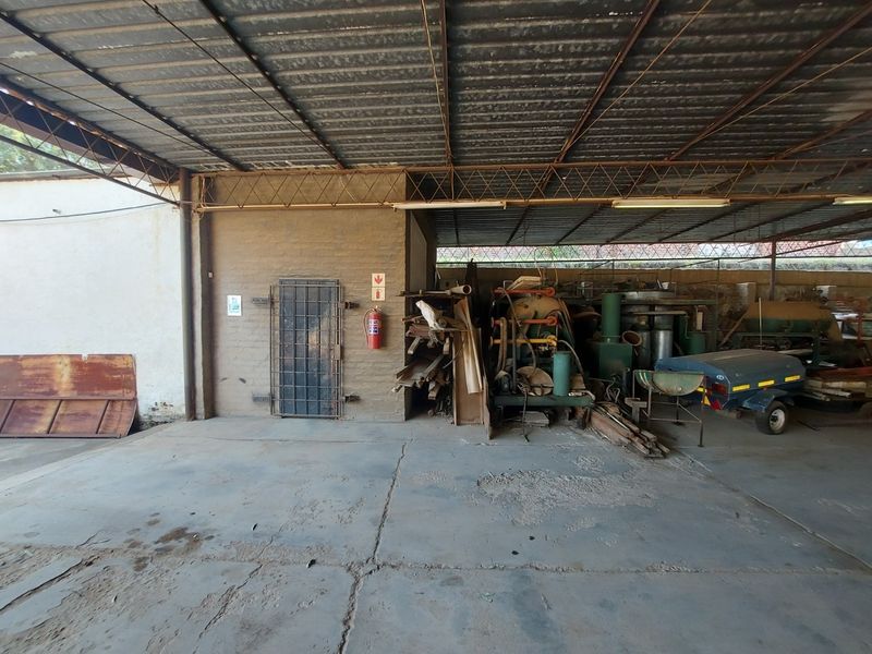 A large, covered industrial-style garage or utility space featuring a concrete floor, steel roof structure, and secure access point.