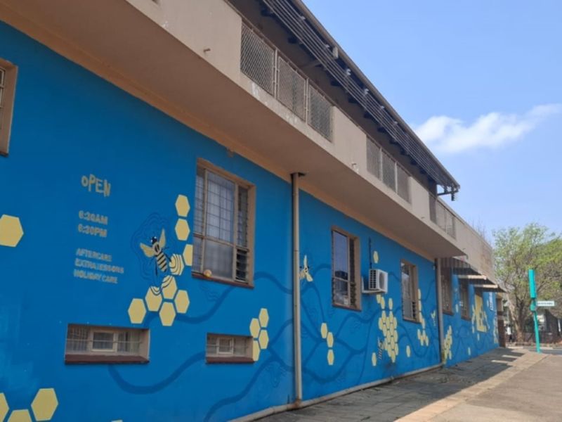 Street-facing commercial building facade featuring a blue painted exterior with decorative mural, security window bars, and an external air conditioning unit.