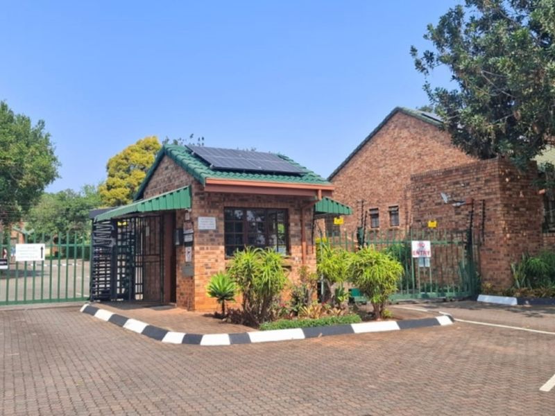 A secure residential estate entrance featuring a brick guardhouse with solar panels, metal security gates, and electric fencing.