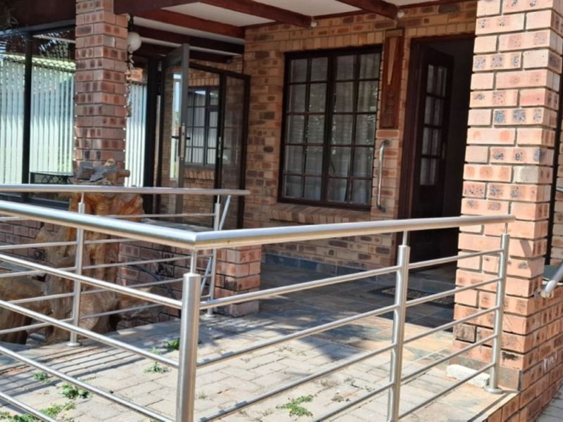 A covered patio area featuring exposed brick pillars, stainless steel balustrades, and paved flooring, providing a functional outdoor entrance space.