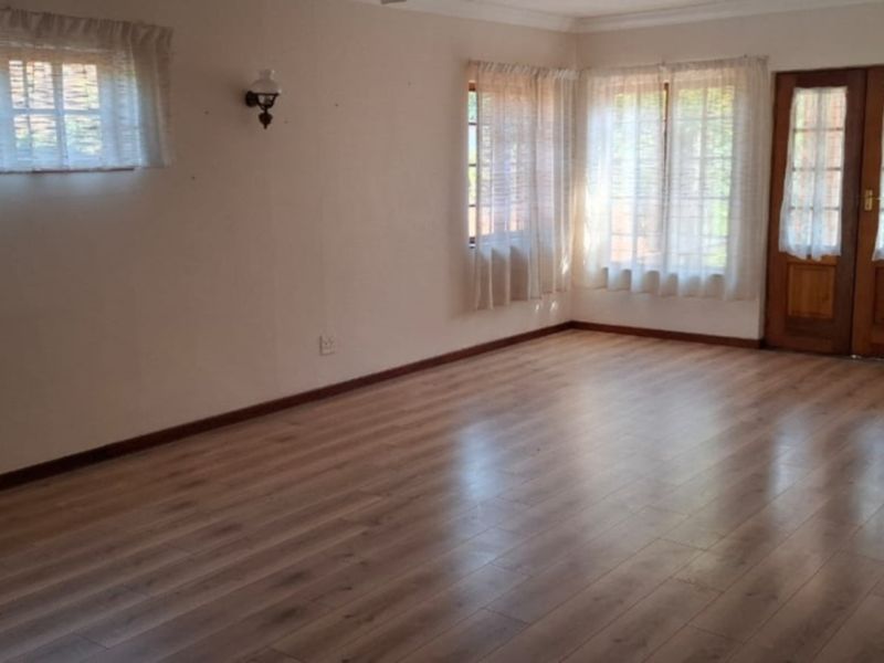 A spacious, empty living room featuring light-toned laminate flooring, neutral walls, and wooden double doors leading to the exterior.