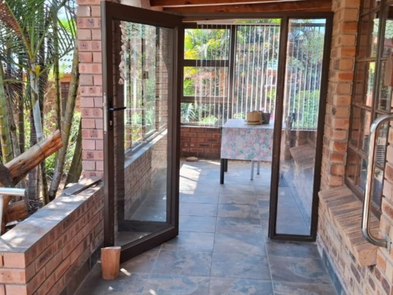A covered patio area featuring exposed brickwork, tiled flooring, and aluminium-framed glass doors leading to an outdoor garden space.