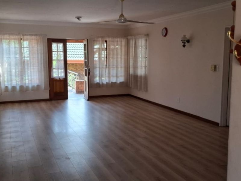 Spacious, light-filled living area featuring laminate flooring, coved cornicing, and direct access to an outdoor space through a timber-framed glass door.