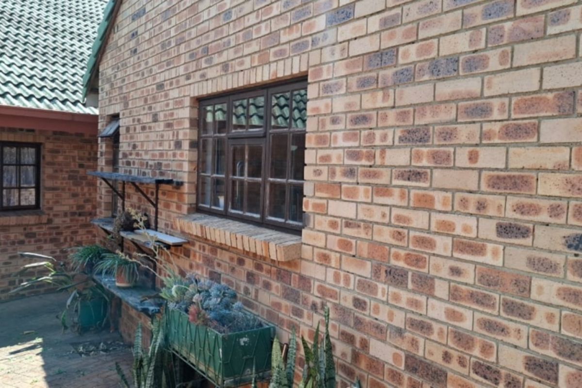 A view of the rear exterior featuring face brick walls, tiled roofing, and metal-framed windows overlooking a paved courtyard area.