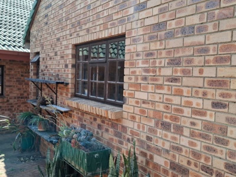 A view of the rear exterior featuring face brick walls, tiled roofing, and metal-framed windows overlooking a paved courtyard area.