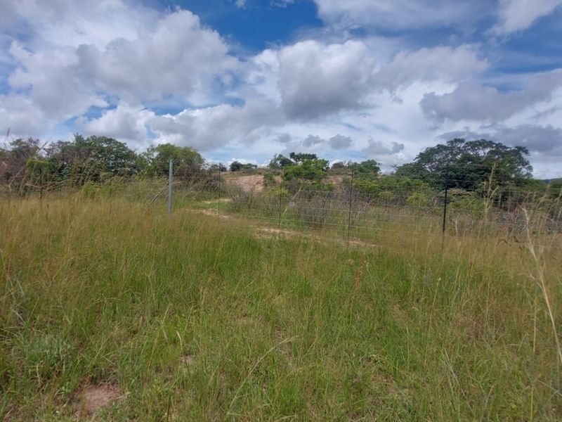 A view of a vacant commercial land plot featuring natural grass terrain and perimeter wire mesh fencing.