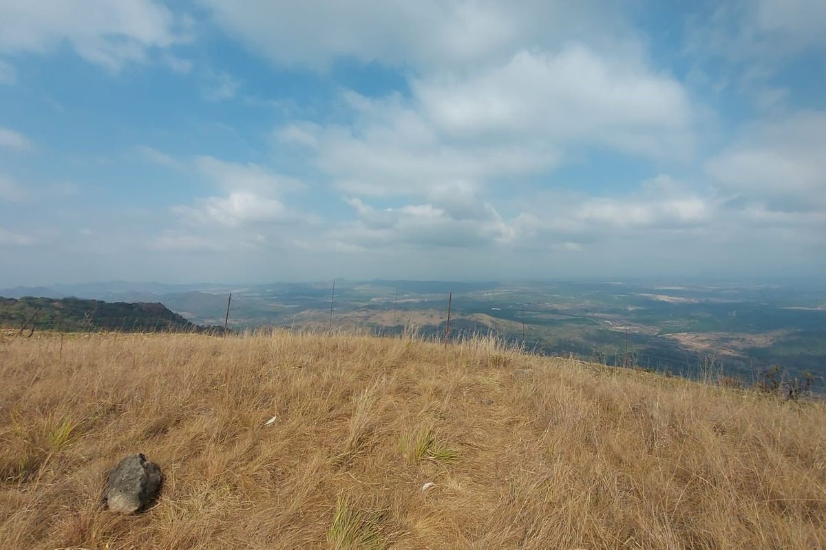 Expansive elevated landscape view overlooking the surrounding farm terrain and distant hills under a blue sky.