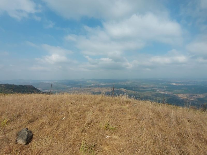 Expansive elevated landscape view overlooking the surrounding farm terrain and distant hills under a blue sky.