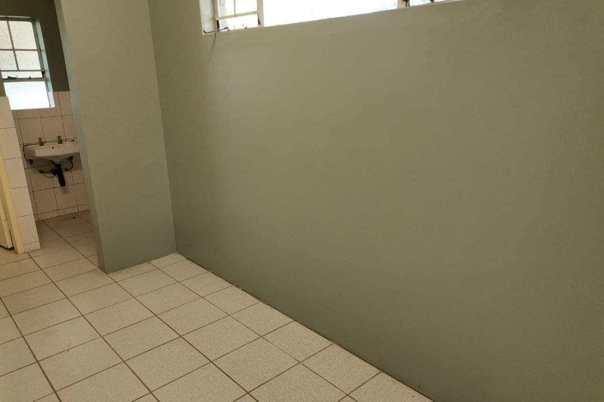 A vacant bathroom space featuring ceramic floor tiles, a wall-mounted basin, and high-level steel-framed windows.
