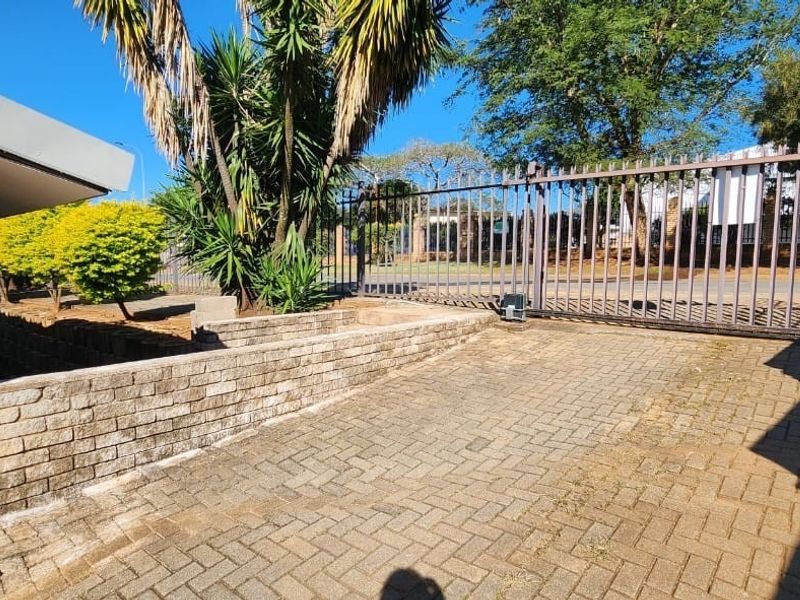 Front entrance area featuring brick paving, a low brick retaining wall, and a secure metal gate providing access to the property.