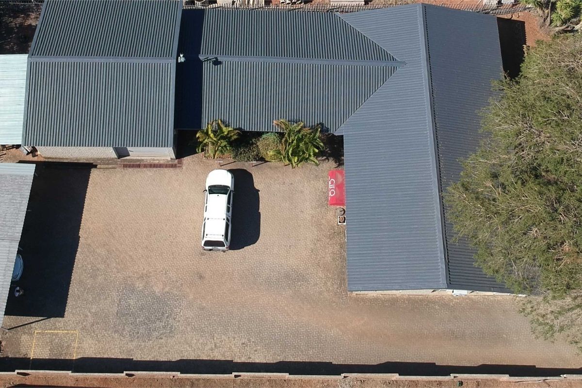 Aerial view of the property showing the main building with a corrugated metal roof, paved parking area, and a carport.