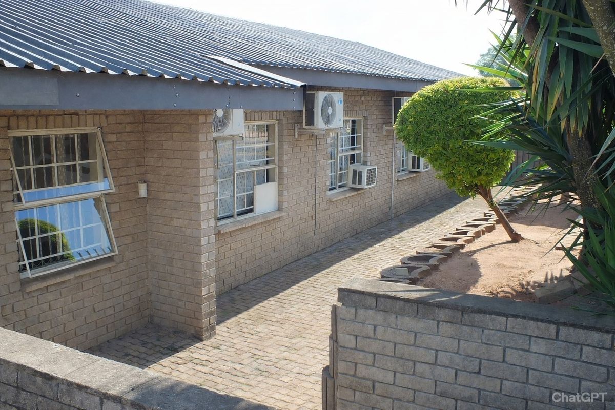 Exterior view of a face brick building featuring a corrugated metal roof, paved walkway, and multiple wall-mounted air conditioning units.