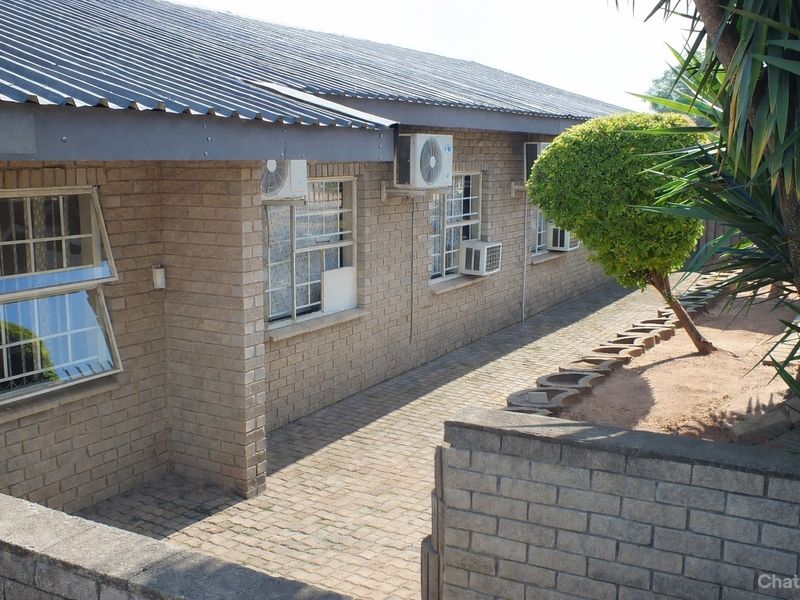 Exterior view of a face brick building featuring a corrugated metal roof, paved walkway, and multiple wall-mounted air conditioning units.