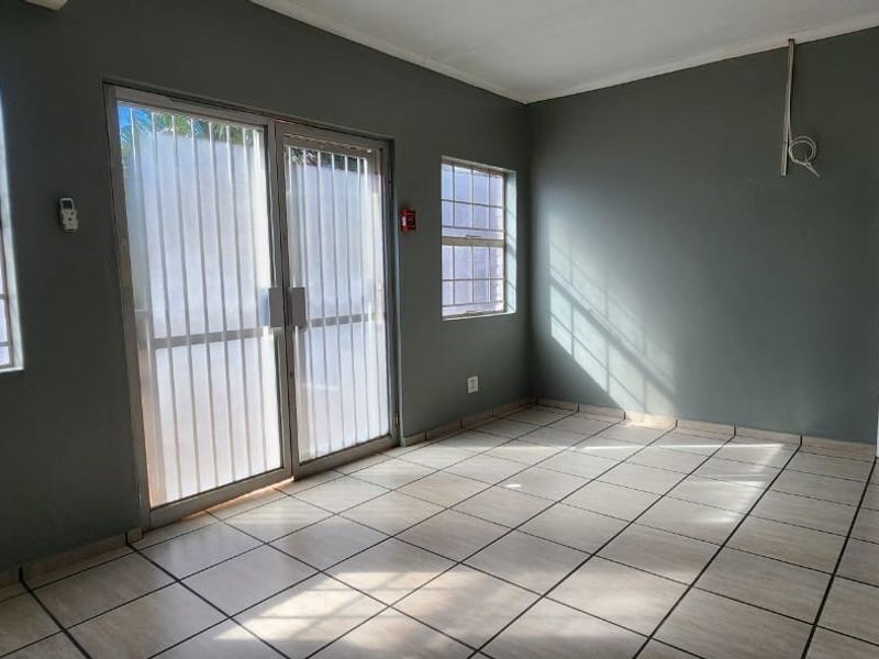 An empty office space featuring tiled flooring, large windows with security bars, and a sliding glass door providing natural light.