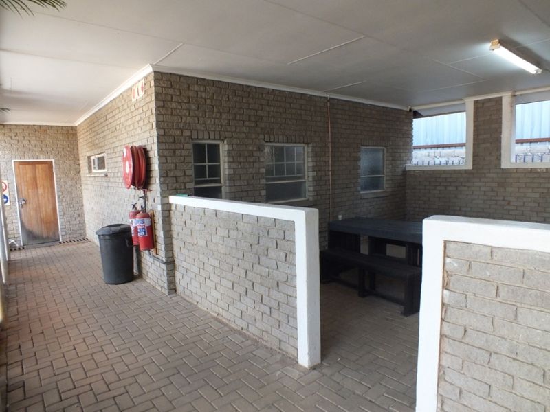 A covered outdoor patio area featuring brick walls, paved flooring, and fixed fire safety equipment, suitable for a functional break or seating space.