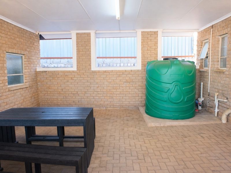 A functional utility space featuring exposed brick walls, paved flooring, and a large integrated water storage tank with plumbing connections.