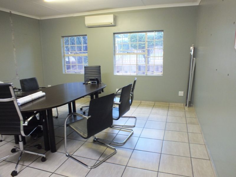 A functional office space featuring tiled flooring, split-system air conditioning, and large windows with security bars, suitable for a professional business environment.