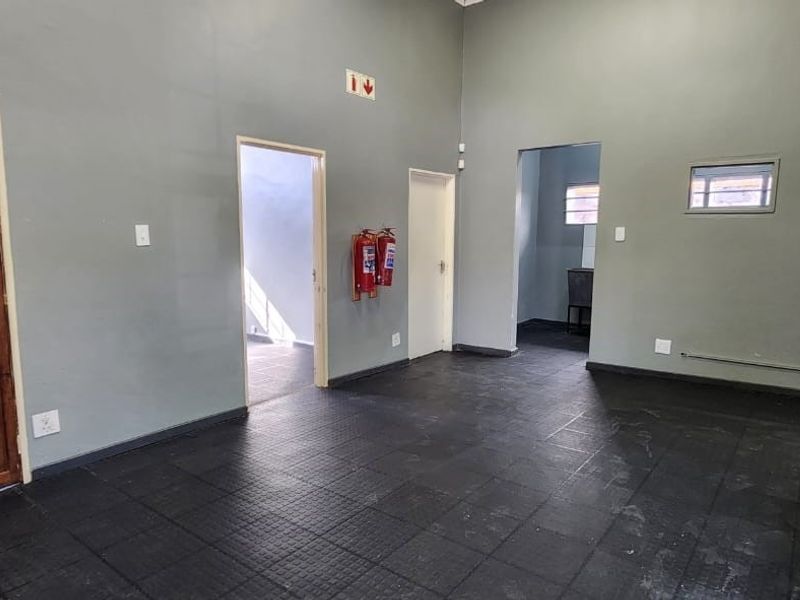 A spacious, empty office area featuring durable rubber flooring, multiple access points, and wall-mounted fire safety equipment.